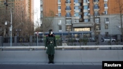 Pripadnik Kineskih narodnih naoružanih policijskih snaga nosi masku dok posmatra ulicu tokom pandemije koronavirusa u Pekingu, 1. decembra 2022.