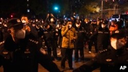 Osoba iz osiguranja u civilnoj odjeći razgovara na telefon dok formira redove policajaca da blokiraju demonstrante u Pekingu 27. studenog 2022.