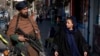 FILE - A Taliban fighter stands guard as a woman walks past in Kabul, Afghanistan, Dec. 26, 2022. 