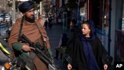 FILE - A Taliban fighter stands guard as a woman walks past in Kabul, Afghanistan, Dec. 26, 2022. 