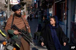 FILE - A Taliban fighter stands guard as a woman walks past in Kabul, Afghanistan, Dec. 26, 2022.