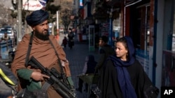 FILE - A Taliban fighter stands guard as a woman walks past in Kabul, Afghanistan, Dec. 26, 2022. 