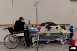 天津南開醫院裡一名坐輪椅的男子守護一名感染新冠的病人。（2022年12月28日）