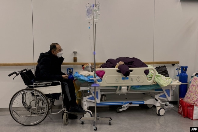 天津南开医院里一名坐轮椅的男子守护一名感染新冠的病人。（2022年12月28日）