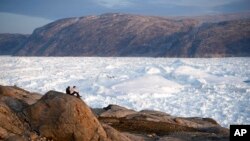 FILE - In this Aug. 16, 2019, photo, student researchers sit on top of a rock overlooking the Helheim glacier in Greenland. 