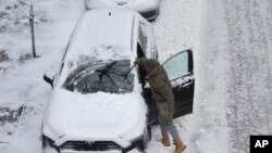 美国艾奥瓦州一名男子在清除汽车上的积雪。（2022年12月22日）