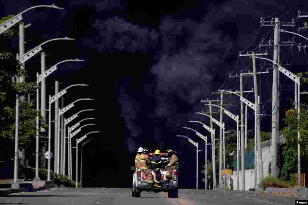 Bombeiros são transportados num carro enquanto o fumo negro sobe durante um incêndio numa área de armazenamento de hidrocarbonetos da empresa Bravo Petroleum em Barranquilla, Colômbia, 21 de dezembro de 2022.