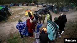 Migrantes que buscan asilo se reúnen alrededor de una fogata para calentarse durante un día de fuertes vientos y bajas temperaturas en un campamento improvisado cerca de la frontera entre EEUU y México, el 23 de diciembre de 2022.