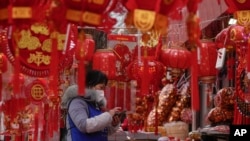 A vendor wearing a face mask checks her smartphone at her store selling Chinese Lunar New Year decorations in Beijing, Jan. 7, 2023. 
