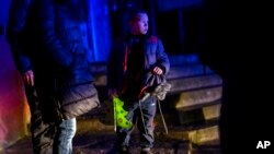 A boy holds a handmade Christmas tree as he waits outside a building that was shelled during a Russian attack in Kherson, southern Ukraine, Nov. 24, 2022.