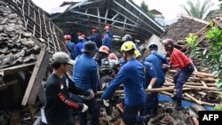 Petugas SAR menurunkan sepeda motor saat bekerja mencari anak hilang yang diyakini terjebak di reruntuhan rumah ambruk di Cugenang, Cianjur, Jawa Barat pada 24 November 2022. (Foto: AFP)