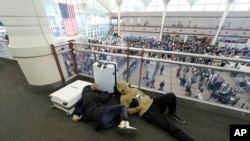 A pair of travelers sleep while fellow travelers queue up below to pass through the south security checkpoint in Denver International Airport, Dec. 23, 2022, in Denver. More than 4,600 flights within, into or out of the U.S. were canceled the same day, according to the tracking site FlightAware.