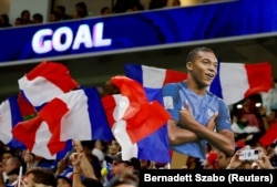 Potongan foto Kylian Mbappe dari Prancis diangkat tinggi-tinggi saat bendera Prancis dikibarkan oleh para penggemar selama pertandingan. (Foto: REUTERS/Bernadett Szabo)