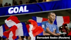 Potongan foto Kylian Mbappe dari Prancis diangkat tinggi-tinggi saat bendera Prancis dikibarkan oleh para penggemar selama pertandingan. (Foto: REUTERS/Bernadett Szabo)