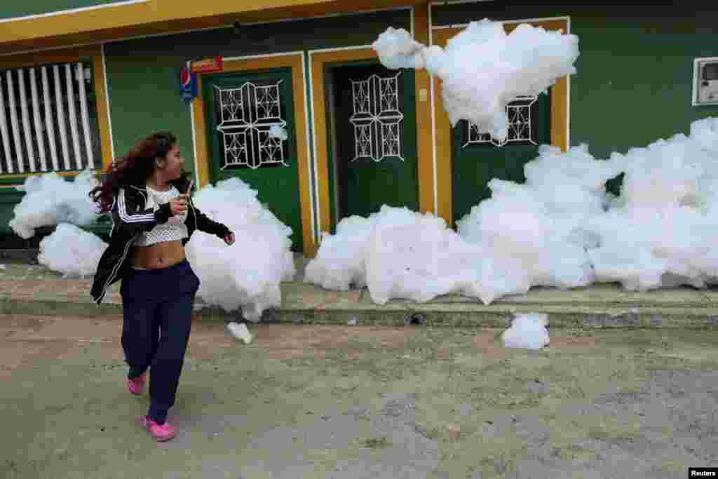 A woman flees from the polluting foam generated by a river full of waste, at the entrance of her house in Mosquera, Colombia, April 27, 2022.