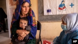 A Save the Children nutrition counsellor, right, explains to Nelab, 22, how to feed her 11-month-old daughter with therapeutic food used to treat severe acute malnutrition, in Sar-e-Pul province of Afghanistan, Sept. 29, 2022. (Save the Children via AP)