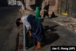 Seorang perempuan dengan gangguan jiwa bersender pada pagar setelah membasahi rambutnya di keran air minum umum, di kawasan Skid Row, Los Angeles.