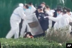 In this photo provided Nov 23, 2022, security personnel in protective clothing surround and kick a protester after he grabbed a metal pole that had been used to strike him during protest at the factory compound operated by Foxconn Technology Group who runs the world's biggest Apple iPhone factory in Zhengzhou in central China's Henan province.