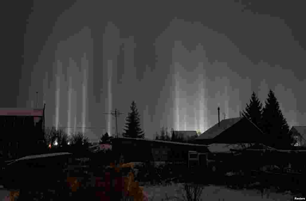 Pillars of light, which are optical atmospheric phenomena, beam up from the ground into the sky behind residential buildings in Omsk, Russia, Jan. 2, 2023. 