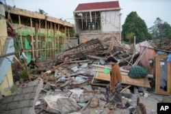 Seorang perempuan berjalan melewati reruntuhan bangunan yang rata dengan tanah akibat gempa Senin di Cianjur, Jawa Barat, Selasa, 22 November 2022. (AP Photo/Tatan Syuflana)
