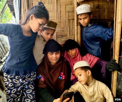 Pengungsi Rohingya Surah Khatoon tampak duduk bersama anak-anaknya ketika berbincang dengan putrinya Sanowara Begum, yang berada di Malaysia, melalui video call, di rumahnya di Cox's Bazar, Bangladesh. (Foto: VOA/Mohammed Rezuwan Khan)