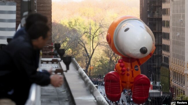 A spectator gets a closer view as Astronaut Snoopy flies by during the 96th Macy's Thanksgiving Day Parade in New York, Nov. 24, 2022.