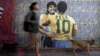 A woman walks her dogs by a wall with an image depicting late football stars Diego Maradona of Argentina and Pele of Brazil embracing each other, in Buenos Aires on Dec. 29, 2022, just hours after the passing of Pele.