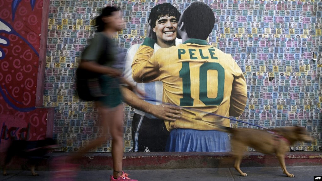 A woman walks her dogs by a wall with an image depicting late football stars Diego Maradona of Argentina and Pele of Brazil embracing each other, in Buenos Aires on Dec. 29, 2022, just hours after the passing of Pele.