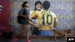 A woman walks her dogs by a wall with an image depicting late football stars Diego Maradona of Argentina and Pele of Brazil embracing each other, in Buenos Aires on Dec. 29, 2022, just hours after the passing of Pele.