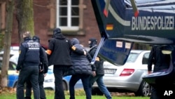 A suspect, second right, is escorted from a police helicopter by police officers after the arrival in Karlsruhe, Germany, Dec. 7, 2022. 