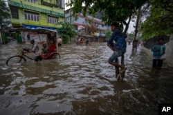 People wade through a flooded road after heavy rains in Gauhati, Assam state, India, on June 14, 2022