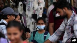 People walk past a girl wearing a face mask in a shopping district of Mumbai, India, Dec. 22, 2022.