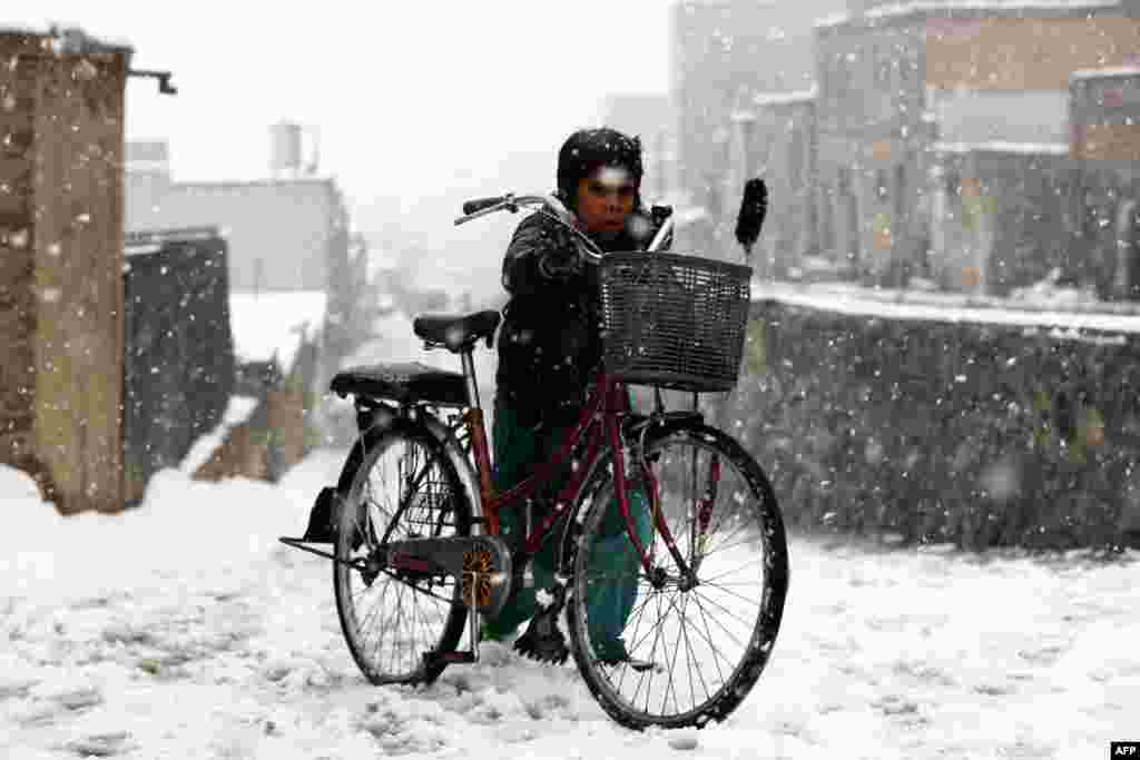 A boy pushes his bicycle along a street during snowfall in Kabul, Afghanistan.