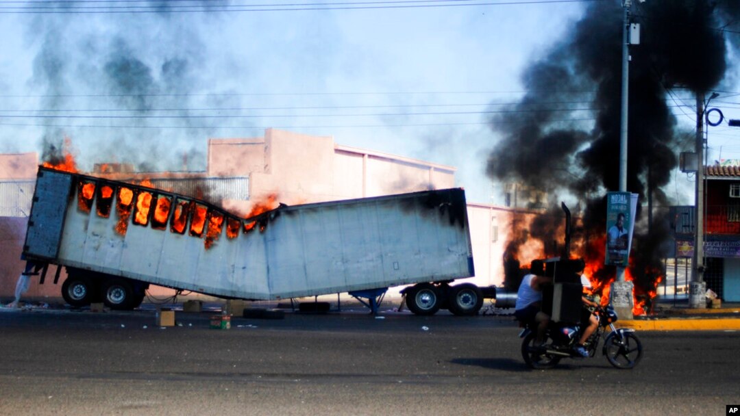 Dos hombres a bordo de una motocicleta pasan junto a un camión en llamas en las calles de Culiacán, en el estado de Sinaloa, el 5 de enero de 2023.