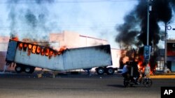 Dos hombres a bordo de una motocicleta pasan junto a un camión en llamas en las calles de Culiacán, en el estado de Sinaloa, el 5 de enero de 2023.