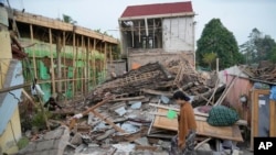 Seorang perempuan berjalan melewati reruntuhan bangunan yang rata dengan tanah akibat gempa Senin di Cianjur, Jawa Barat, Selasa, 22 November 2022. (AP/Tatan Syuflana)