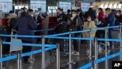 Masked travellers with luggage line up at the international flight check in counter at the Beijing Capital International Airport in Beijing, Thursday, Dec. 29, 2022. 