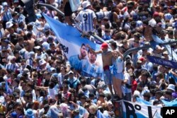 Argentine soccer fans gather near a banner with photos of soccer stars Lionel Messi and Diego Maradona for a parade to honor the team that won the World Cup, in Buenos Aires, Dec. 20, 2022.
