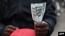 FILE: A man holds a Ghana currency note in Accra, Ghana, on December 1, 2022. On December 14, 2022 Ghana signed a $3 billion bailout deal with the International Monetary Fund in a bid to shore up its public finances, but economic stability is still a way off.