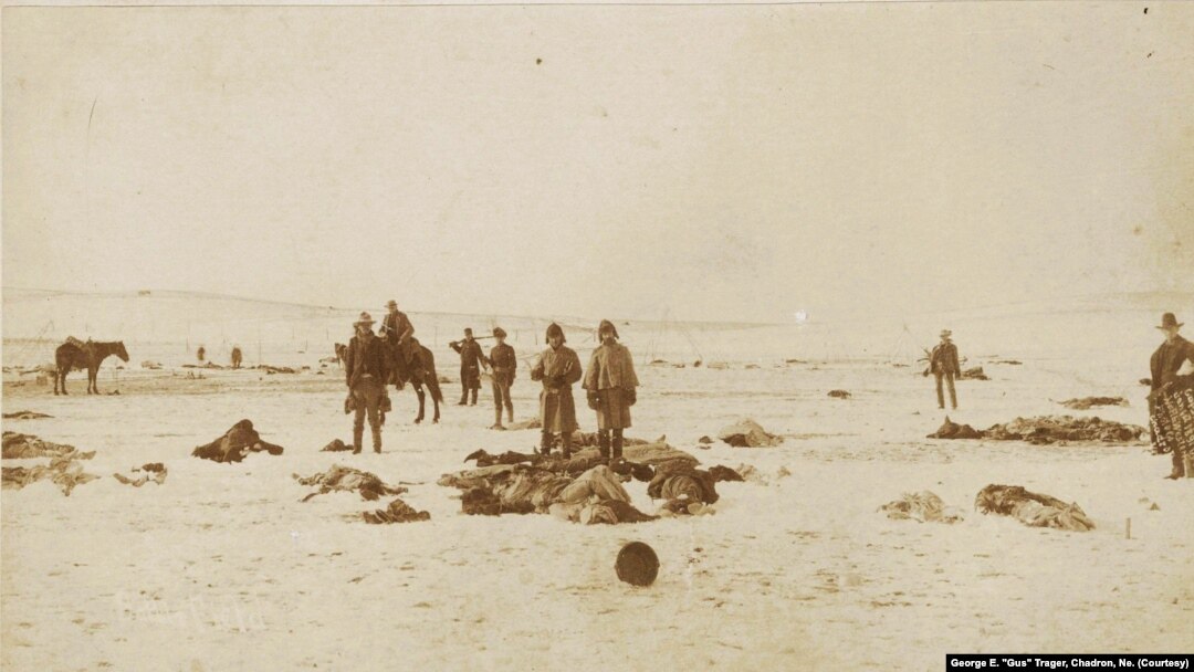 This George E. "Gus" Trager photograph shows soldiers holding moccasins and other items they have looted from the dead at the Wounded Knee Massacre site, 1890.