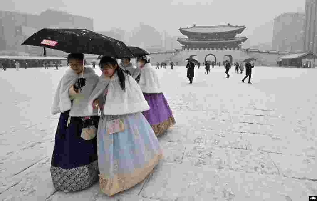 Visitors wearing traditional hanbok dress walk through Gyeongbokgung palace during snowfall in central Seoul, South Korea.