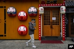 A resident passes by a shuttered restaurant in Beijing, Nov. 24, 2022. China is expanding lockdowns as its numbers of COVID-19 cases have climbed.