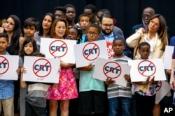 FILE - Children holding signs against Critical Race Theory stand on stage near Florida Gov. Ron DeSantis as he addresses the crowd before publicly signing HB7 at Mater Academy Charter Middle/High School in Hialeah Gardens, Fla., on April 22, 2022. (Daniel A. Varela/Miami Herald via AP, file)