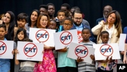 FILE: Kids holding signs against Critical Race Theory stand on stage near Florida Gov. Ron DeSantis as he addresses the crowd before publicly signing HB7 at Mater Academy Charter Middle/High School in Hialeah Gardens, Fla., on April 22, 2022.