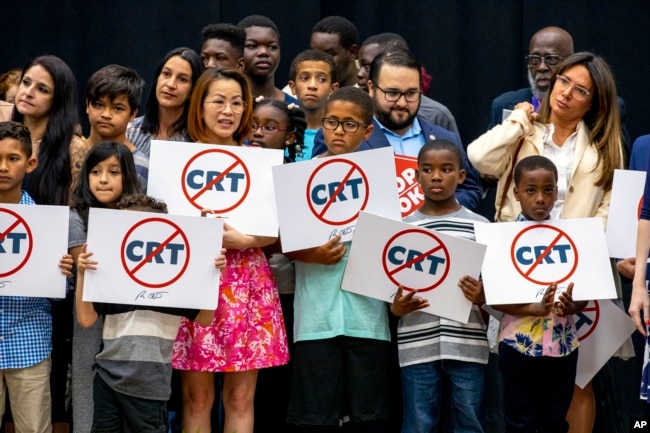 FILE - Kids holding signs against Critical Race Theory stand on stage near Florida Gov. Ron DeSantis as he addresses the crowd before publicly signing HB7 at Mater Academy Charter Middle/High School in Hialeah Gardens, Fla., on April 22, 2022. (Daniel A. Varela/Miami Herald via AP, file) Link Size Keep aspect ratio