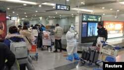 Passengers arriving on international flights wait in line next to a staff member wearing personal protective equipment (PPE) at the airport in Chengdu, China, Jan. 6, 2023. 