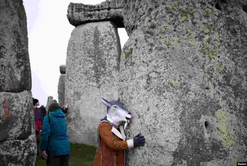 A person wearing an animal mask touches the stones during winter solstice celebrations at Stonehenge near Amesbury, Britain.