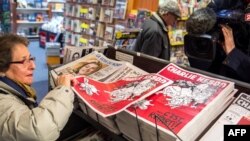 FILE - A woman picks up a copy of the French satirical weekly magazine Charlie Hebdo at a newsstand on Feb. 25, 2015, in Lille.