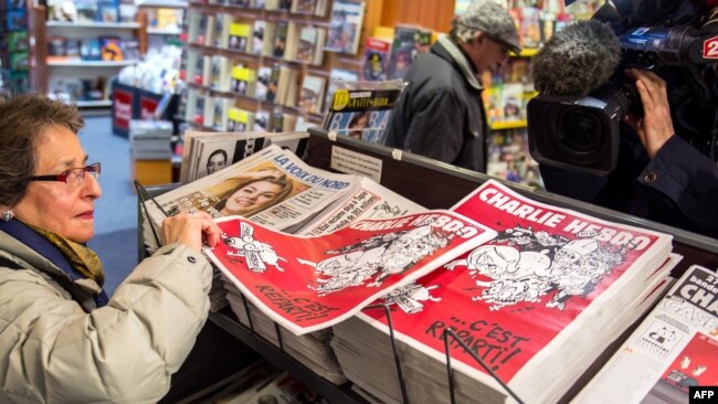 FILE - A woman picks up a copy of the French satirical weekly magazine Charlie Hebdo at a newsstand on Feb. 25, 2015, in Lille.