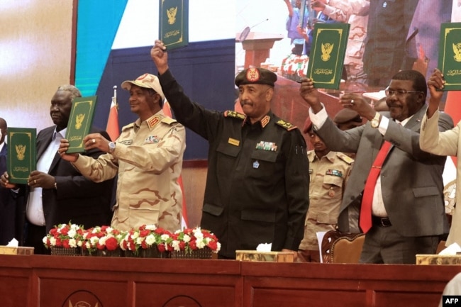 FILE - Sudan's Army chief Abdel Fattah al-Burhan (C R) and paramilitary commander Mohamed Hamdan Dagalo (C L) lift documents alongside civilian leaders following the signing of an initial deal aimed at ending a deep crisis caused by last year's military coup, in the capital Khartoum on December 5, 2022. (Photo by ASHRAF SHAZLY / AFP)